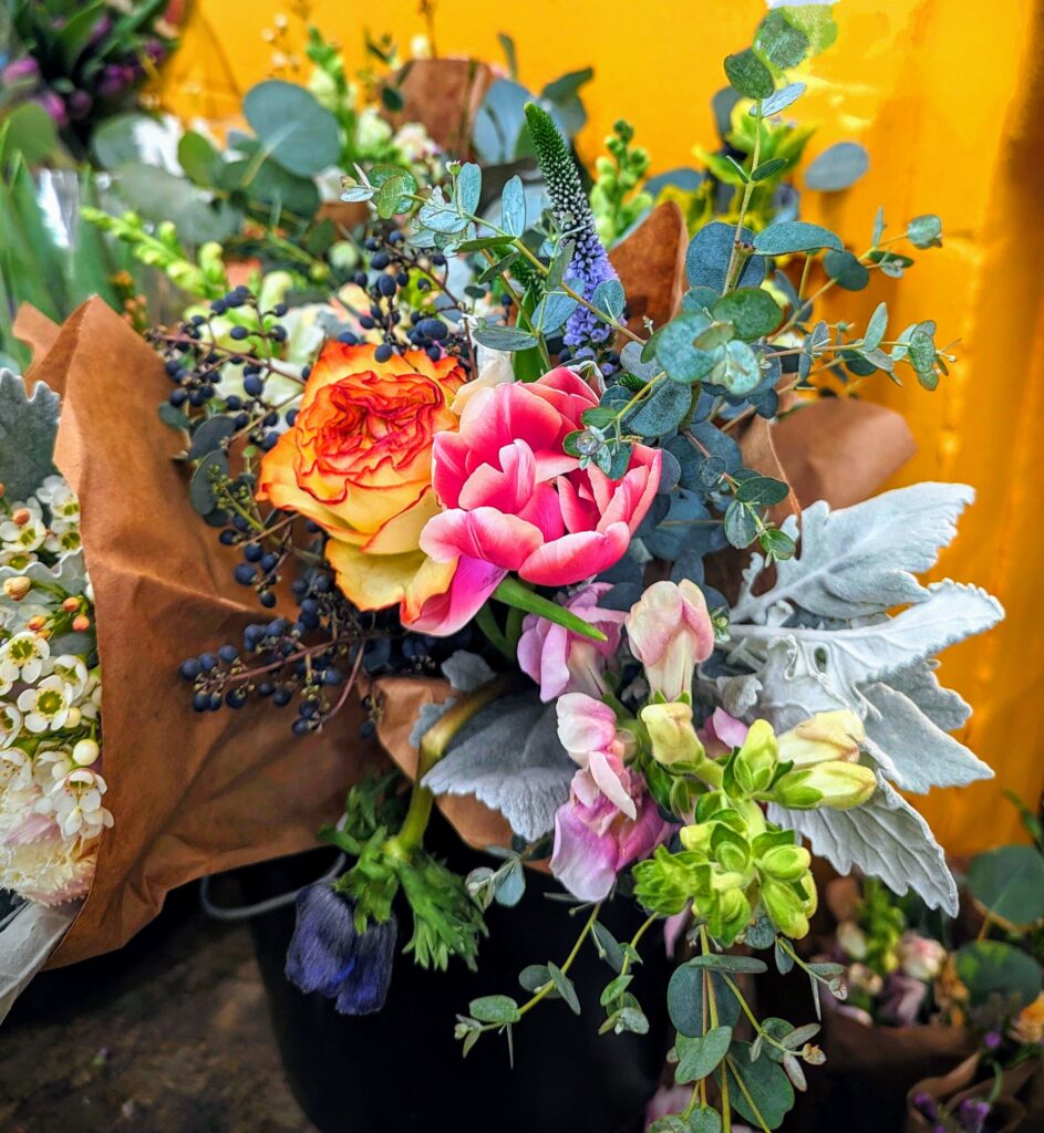 Close up of seasonal bouquet featuring orange, pink, and purple flowers with greenery like eucalyptus.